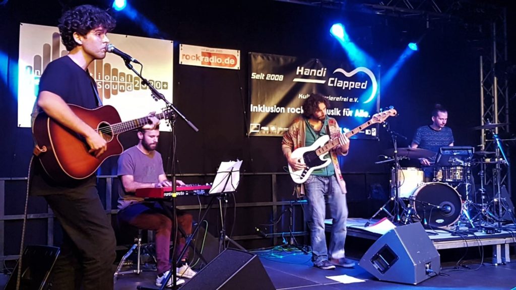 Die vier Mitglieder dar Band Leo Grande live auf der Bühne, mit Gitarre, E-Gitarre, Keyboard und Schlagzeug, im  Hintergrund Handiclapped Banner.